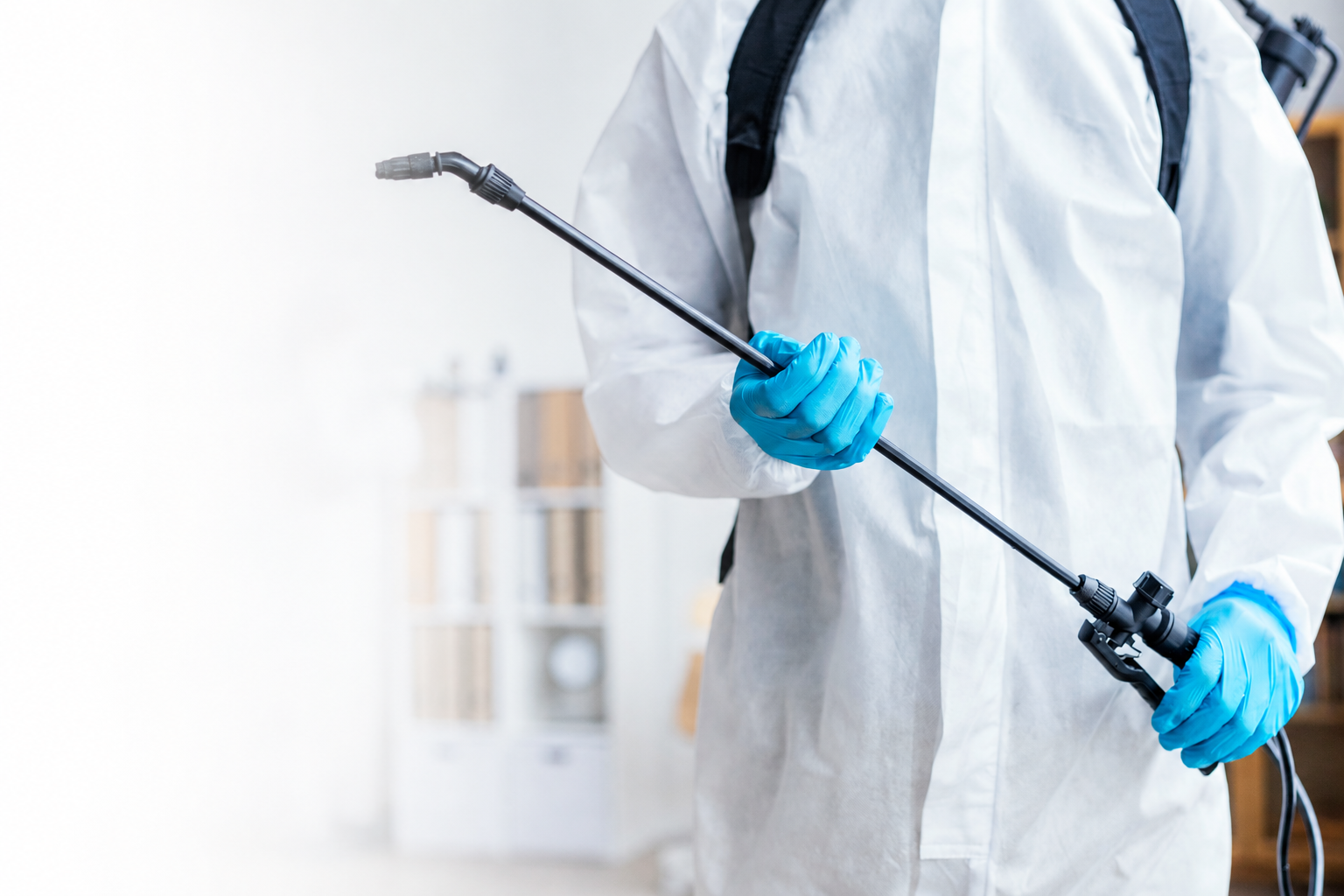 Imagem ilustrativa de profissional de dedetização com roupa de proteção e luvas aplicando produto com pulverizador